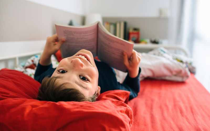Young boy lying upside down and holding a book